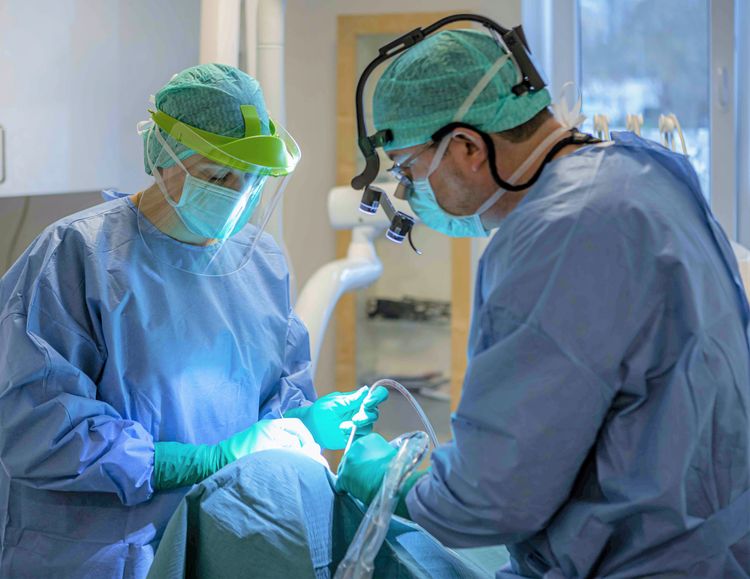 Tandsköterska ochtandläkare i blå operationsrockar, visir, munskydd